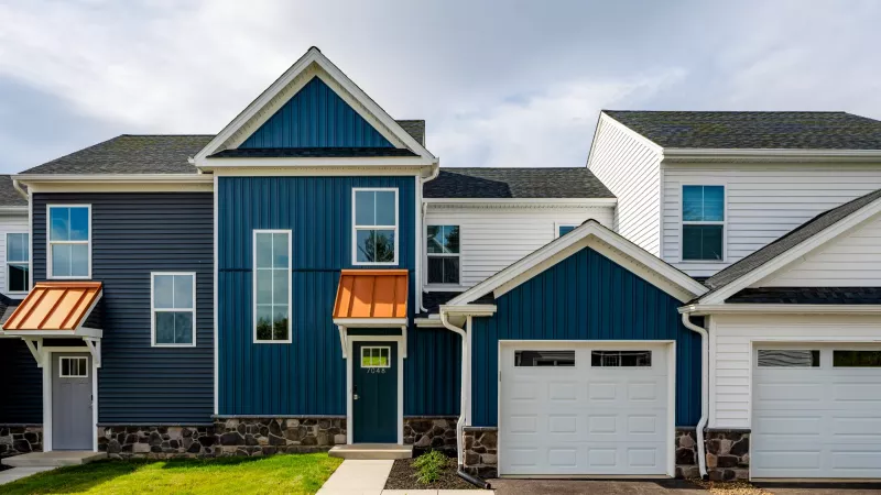 Modern townhome exterior with blue and white siding, orange metal awnings, and attached garage on a sunny day.