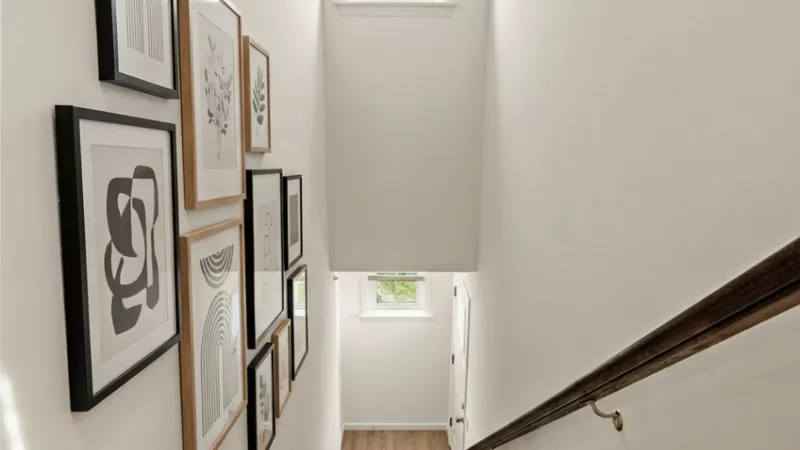 Looking down a bright carpeted staircase with a gallery wall of framed abstract art on the left and a window above.