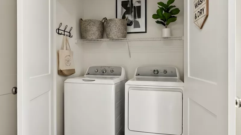 White washer and dryer in a bright laundry closet with open bifold doors, wood floor, and decorative shelf.