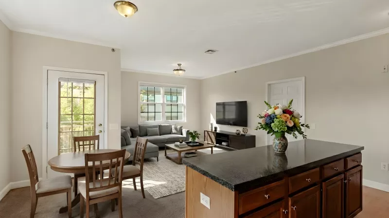 Open-plan living room and kitchen featuring a dark island, round dining table, gray sofa, and colorful flower arrangement.