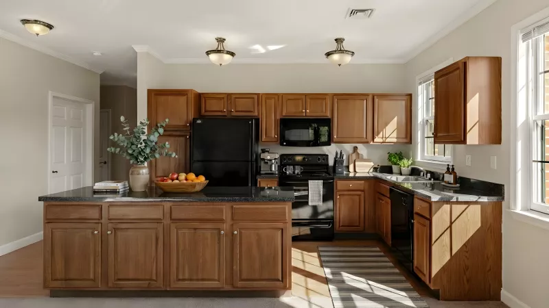 Modern kitchen with warm wood cabinets, black appliances, dark countertops, and a central island. Sunlight streams in.
