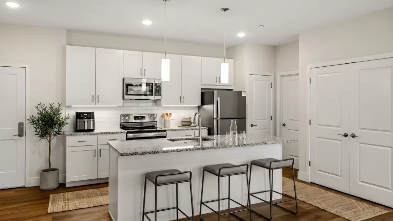 Modern kitchen with white cabinets, dark appliances, a granite island with three bar stools, and wood floors.