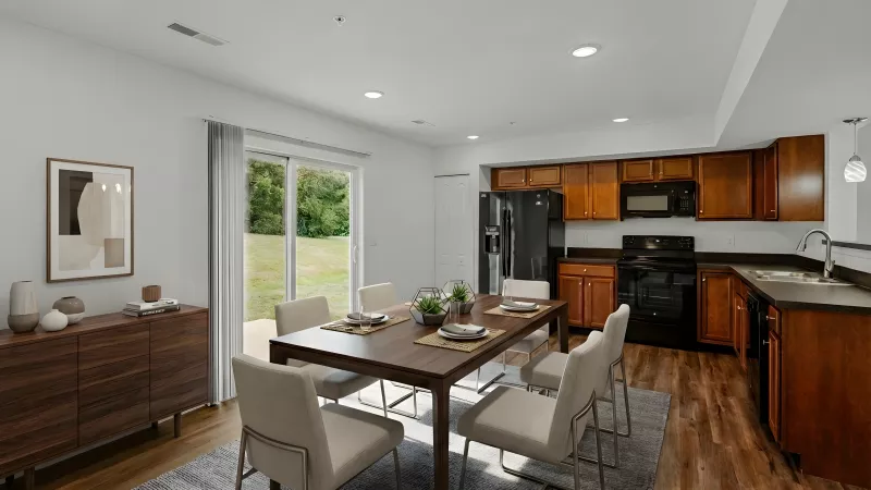 Modern dining room and kitchen with dark wood table, light chairs, and black kitchen appliances.