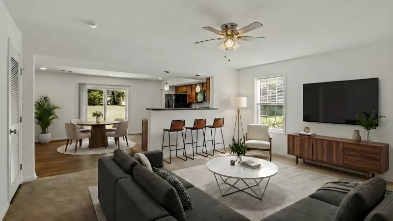 Spacious living room with gray sectional, round coffee table, TV, kitchen island, and dining area.