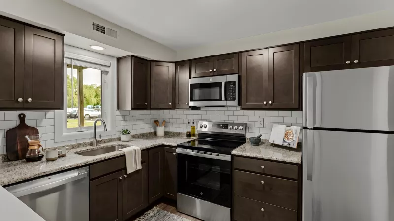 Modern kitchen with dark brown cabinets, stainless steel appliances, light granite countertops, and white subway tile backsplash.
