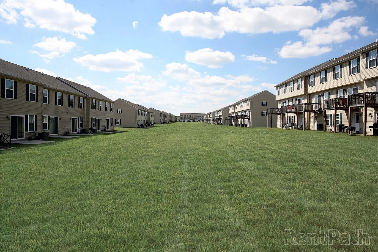 Wide open green space between townhome-style apartment buildings at Keystone Arms in Carlisle, PA, ideal for outdoor recreation, pets, and community gatherings under a bright blue sky.