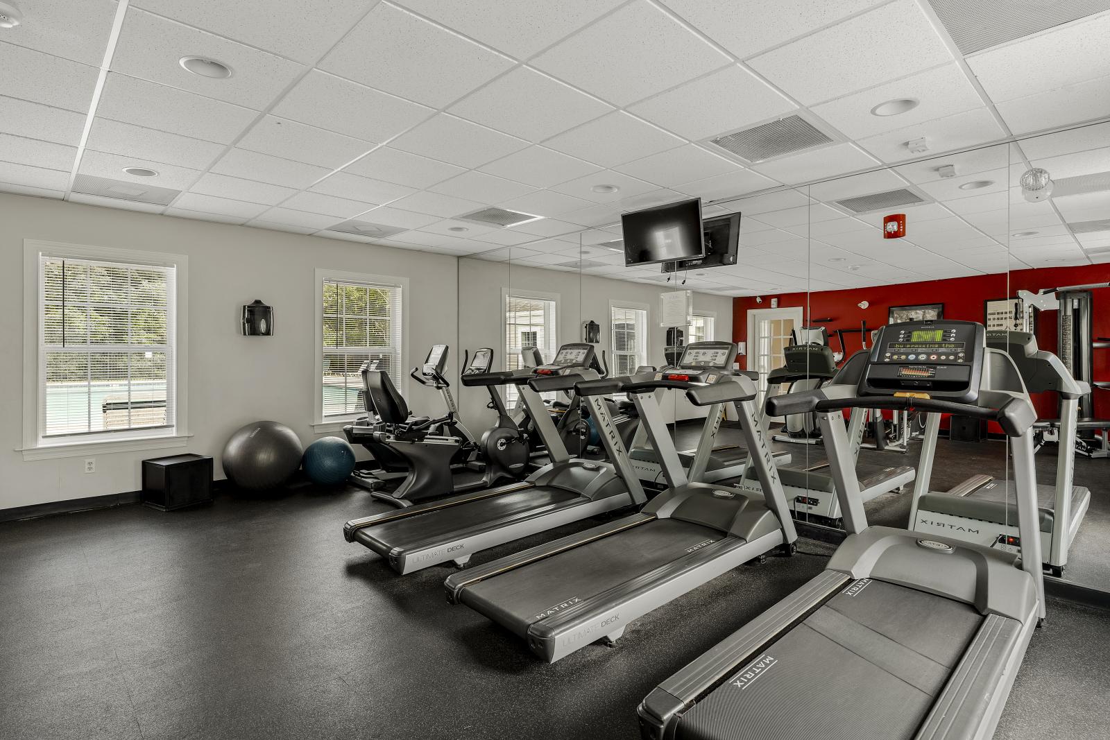 The resident fitness center at Keystone Arms in Carlisle, PA, showcasing a variety of modern cardio and weight training equipment, including treadmills, stationary bikes, and a weight bench. The room is well-lit with large windows and a mirrored wall.