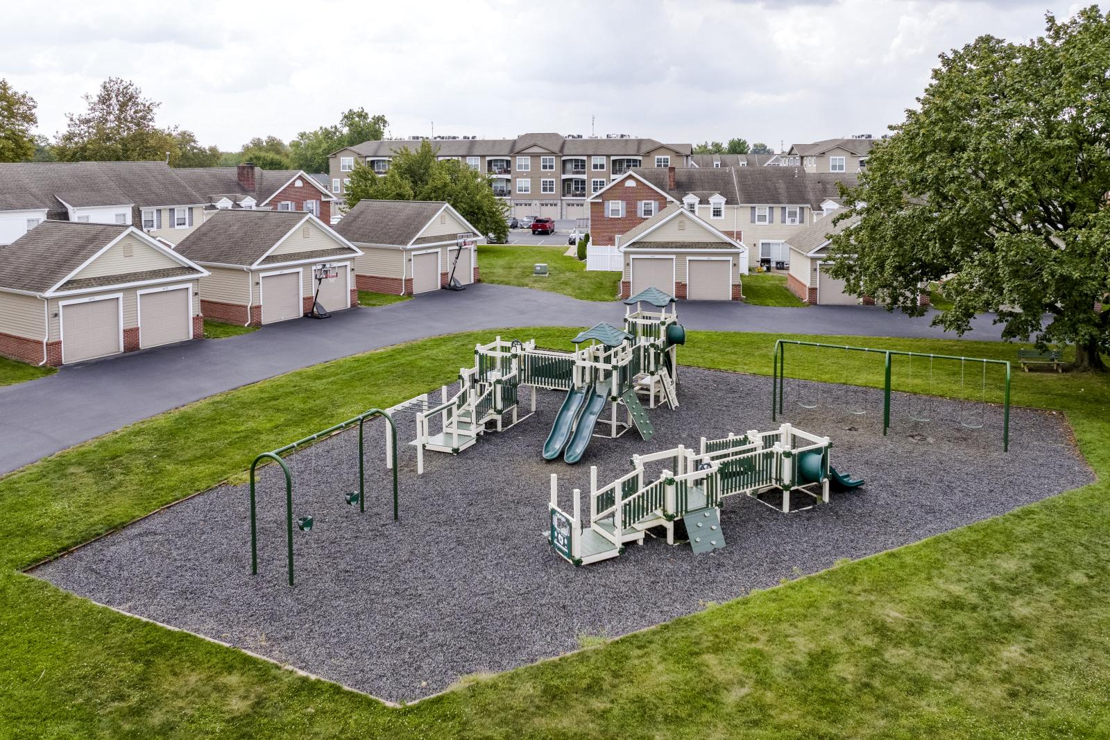 Aerial view of spacious apartment townhomes surrounded by open green lawns, tree-lined streets, and community parking areas.