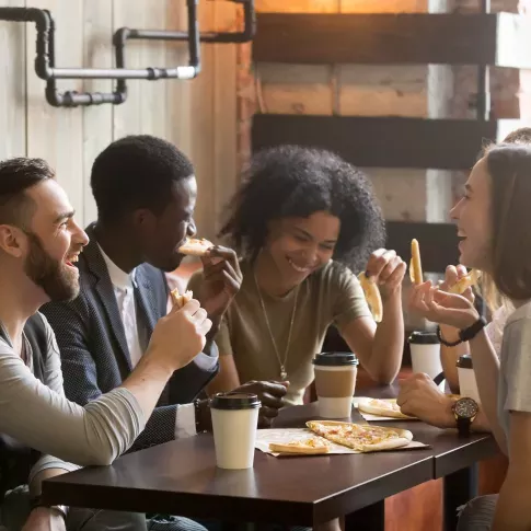 A group of friends enjoying food and coffee together in a cozy indoor setting with warm, rustic decor.