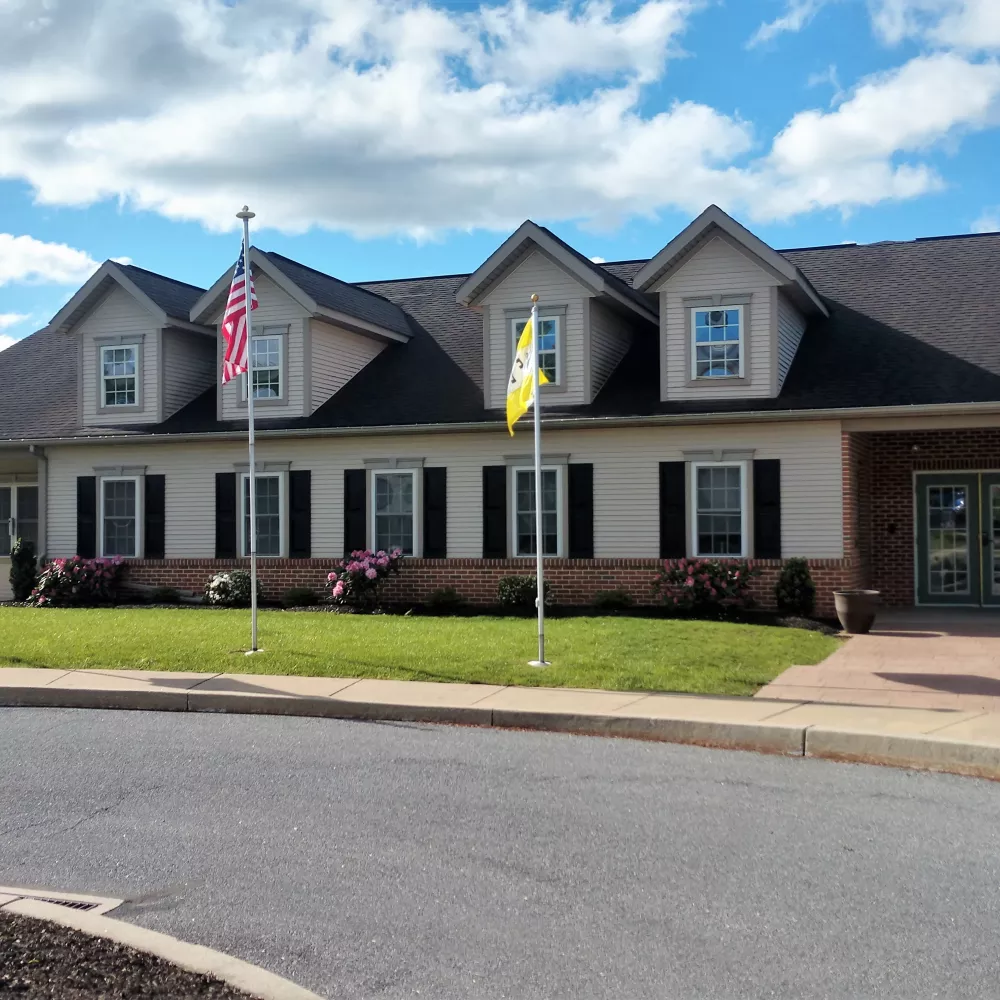 Community clubhouse building with American and welcome flags, surrounded by green lawn and colorful flowers at Newport Commons.