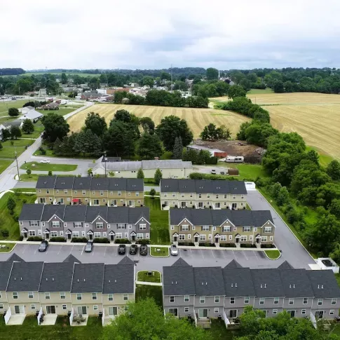 Aerial view of Hunters Pointe townhome apartments in a peaceful rural setting in Pennsylvania, featuring multiple rows of charming two-story residences with green space, parking, and surrounding farmland and trees.