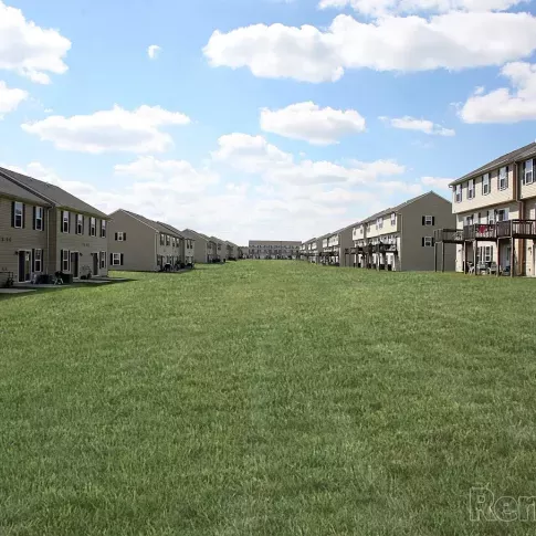 Wide open green space between townhome-style apartment buildings at Keystone Arms in Carlisle, PA, ideal for outdoor recreation, pets, and community gatherings under a bright blue sky.