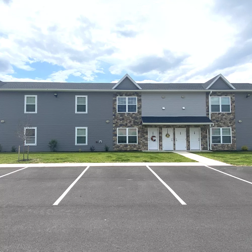 Exterior view of the TownsEdge Apartments building, showcasing modern grey siding, stone accents, multiple windows, and a paved parking lot in front.