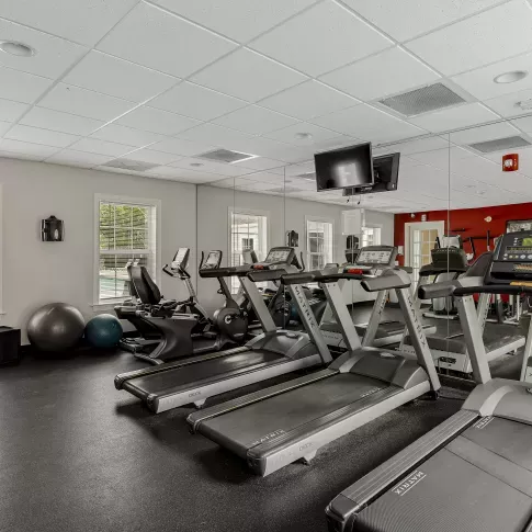 The resident fitness center at Keystone Arms in Carlisle, PA, showcasing a variety of modern cardio and weight training equipment, including treadmills, stationary bikes, and a weight bench. The room is well-lit with large windows and a mirrored wall.