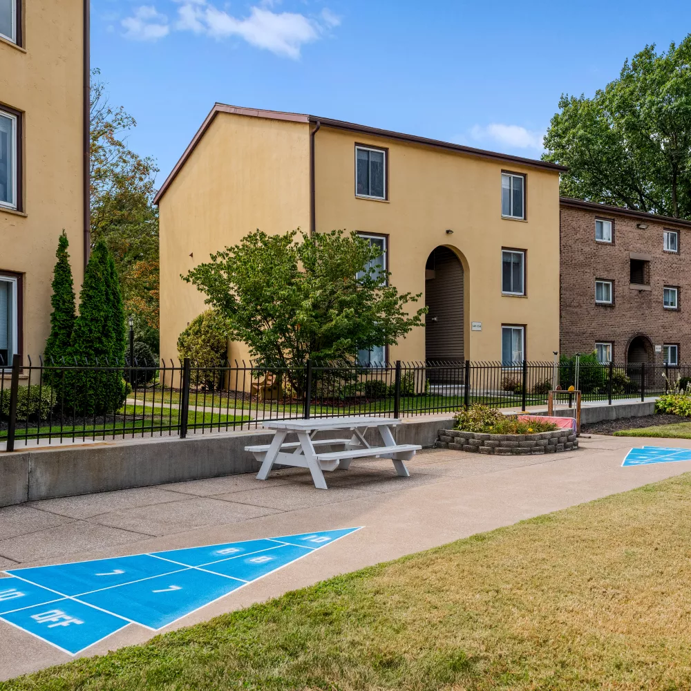 Outdoor shuffleboard court and picnic area with table at Rosedale Apartments, surrounded by landscaped grounds