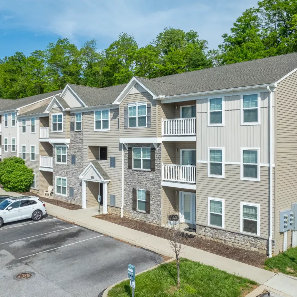 Wyndham Pointe Apartments three-story residential building with stone and beige siding, landscaped entrance, and adjacent parking area under clear blue sky.