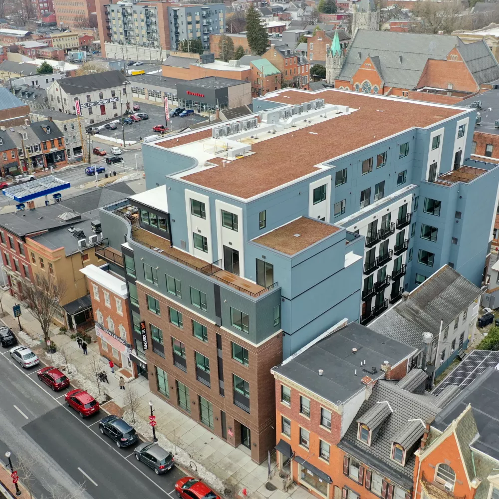 Aerial photograph shows a modern blue and white building contrasting with older brick structures along a city street.