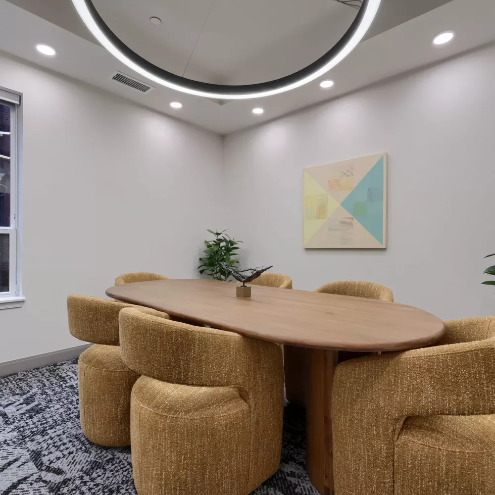 Contemporary meeting room with an oval wooden table, six textured golden-brown chairs, geometric wall art, and plants.