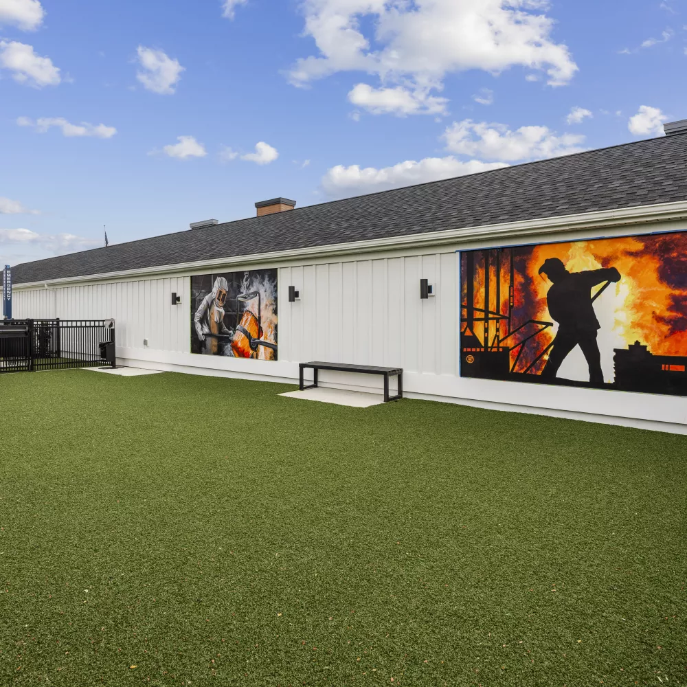 Turf dog park by a white building with two large, vibrant murals