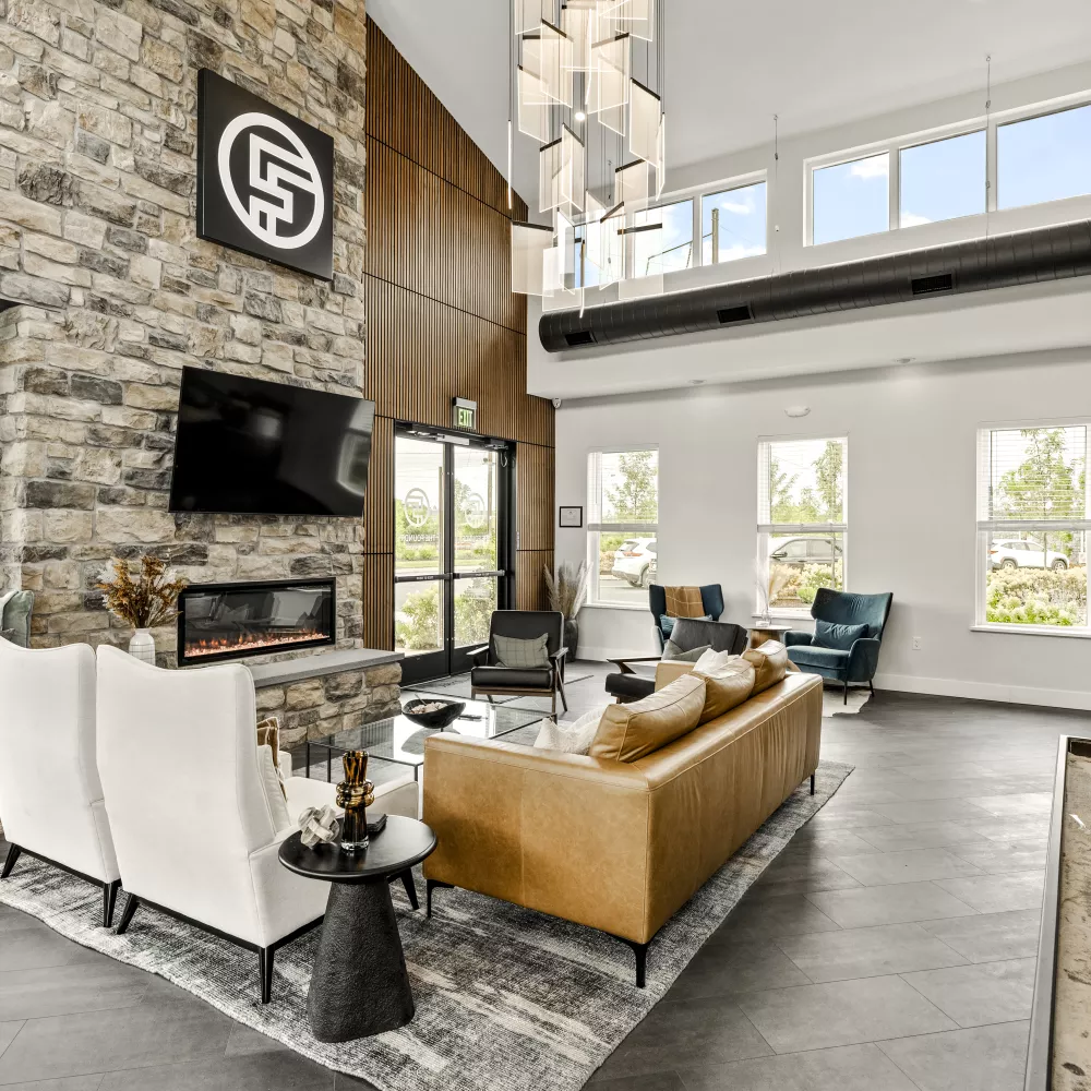 Spacious, modern lounge with a stone accent wall, fireplace, diverse seating, high windows, and a shuffleboard table.