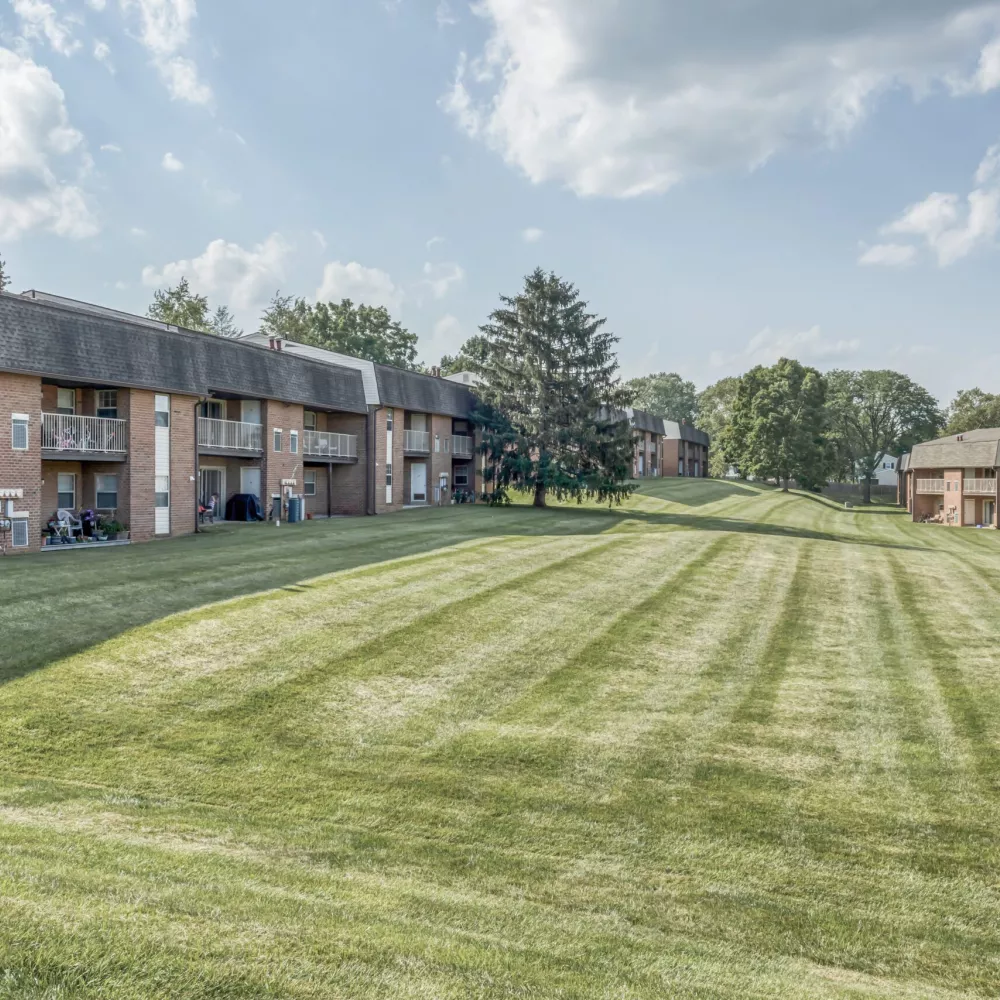 Wide green lawn stretching between two brick apartment buildings with balconies on a sunny day.