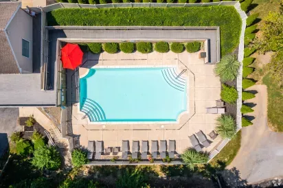 Aerial view of the Mill Creek Manor outdoor pool area with lounge chairs, red umbrella, and privacy landscaping