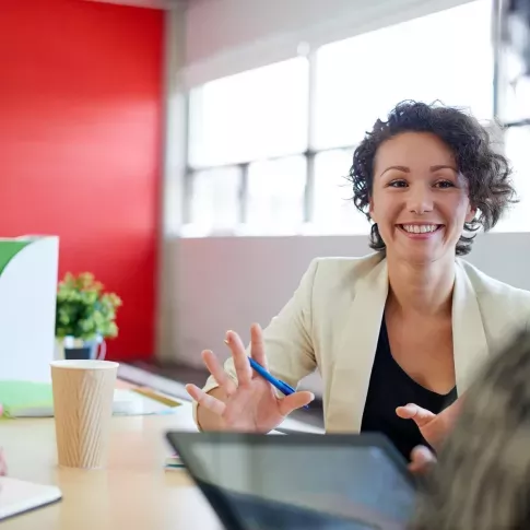 Smiling professional woman engaged in a conversation at a brightly lit office table, conveying a positive and collaborative work environment.