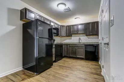 Renovated kitchen at Mill Creek Manor featuring dark wood cabinets, black appliances, granite countertops, and white subway tile backsplash.