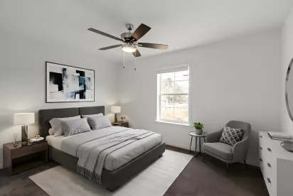 A second bedroom featuring a large window, neutral tones, and a dark grey upholstered bed frame. A ceiling fan and minimalist artwork complete the space.