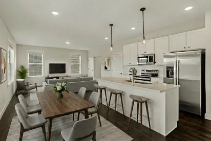 Open-plan living room, dining area, and modern kitchen with white cabinets, stainless steel appliances, and dark wood floors.