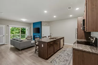 Open-concept living room with a grey sofa, blue accent wall with TV, and kitchen island with granite counters.