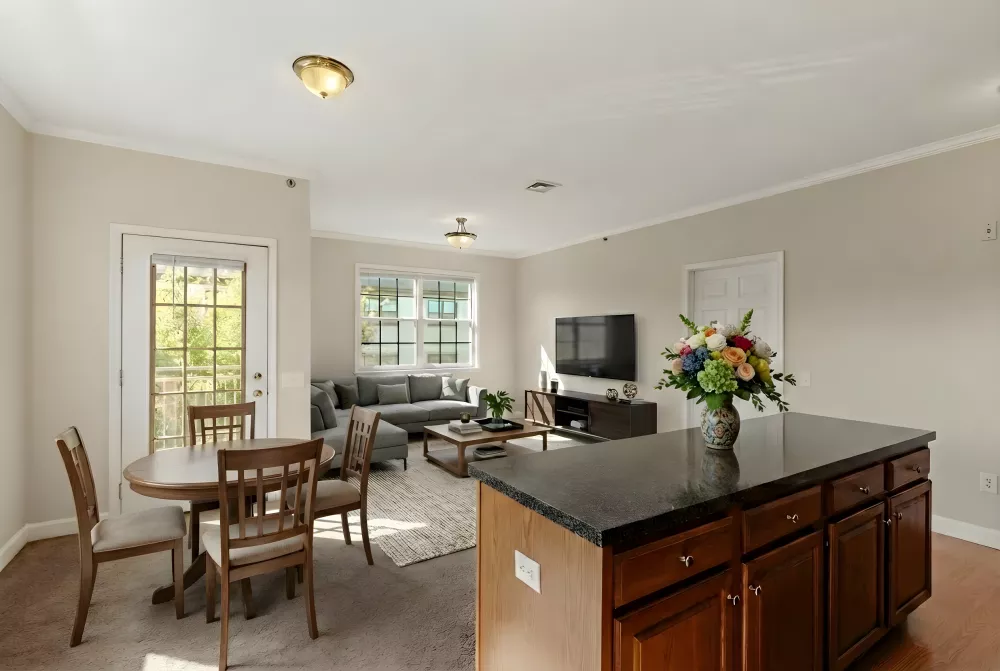 Open-plan living room and kitchen featuring a dark island, round dining table, gray sofa, and colorful flower arrangement.