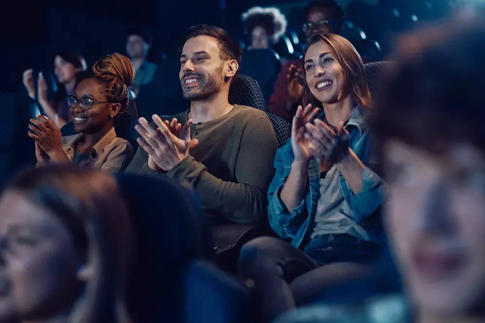  Diverse group of people in a dark movie theater, smiling and clapping with excitement.