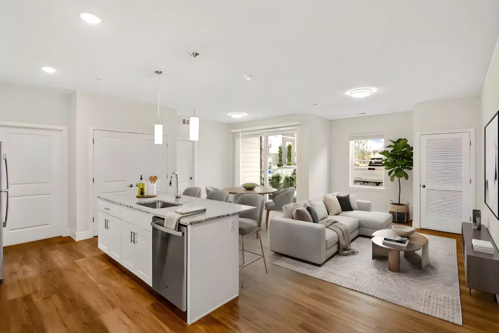 Modern open-plan kitchen, dining, and living room with white cabinets, gray sectional sofa, and hardwood floors.