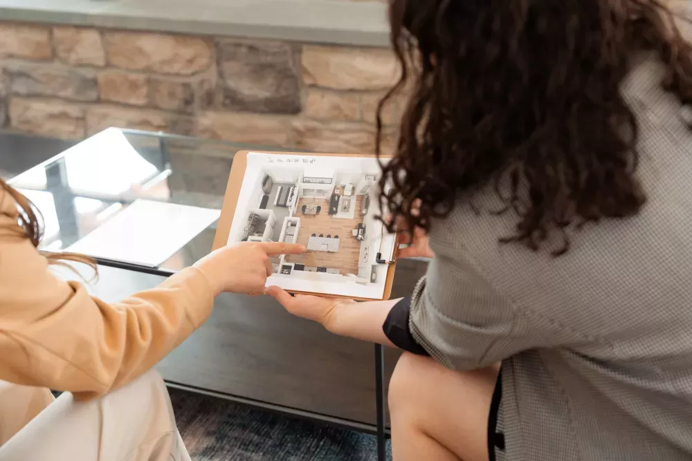 Two women examine a display of plans, one woman points to a specific detail.