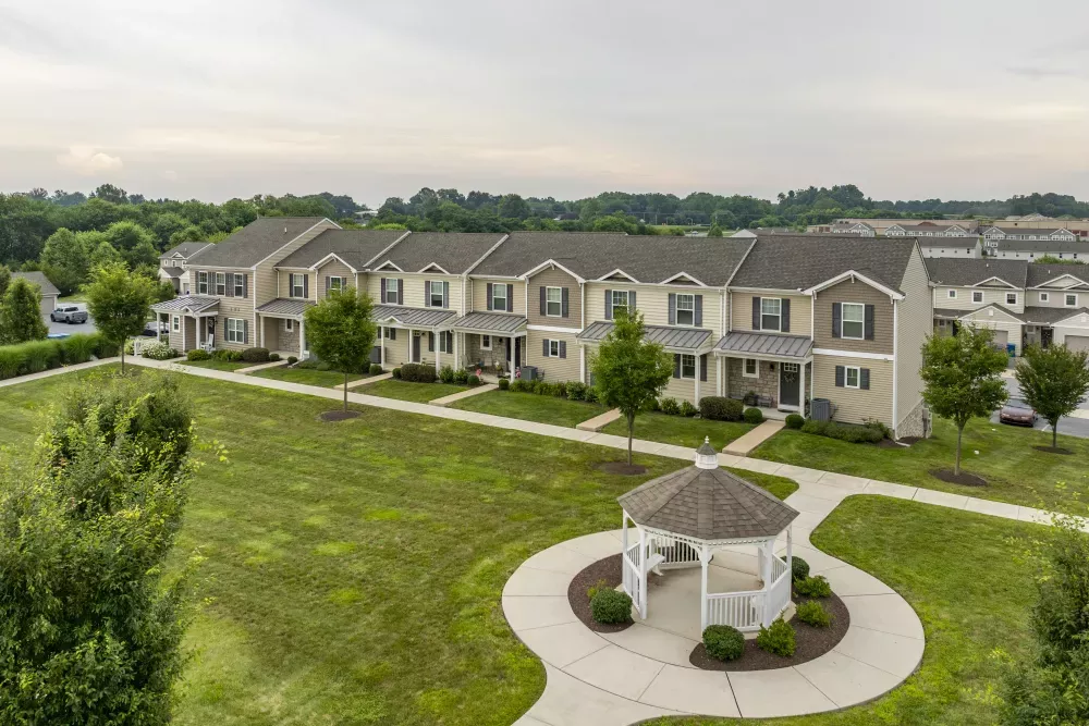 Aerial view of modern townhouses next to a green common area with a white gazebo and paved circular path.