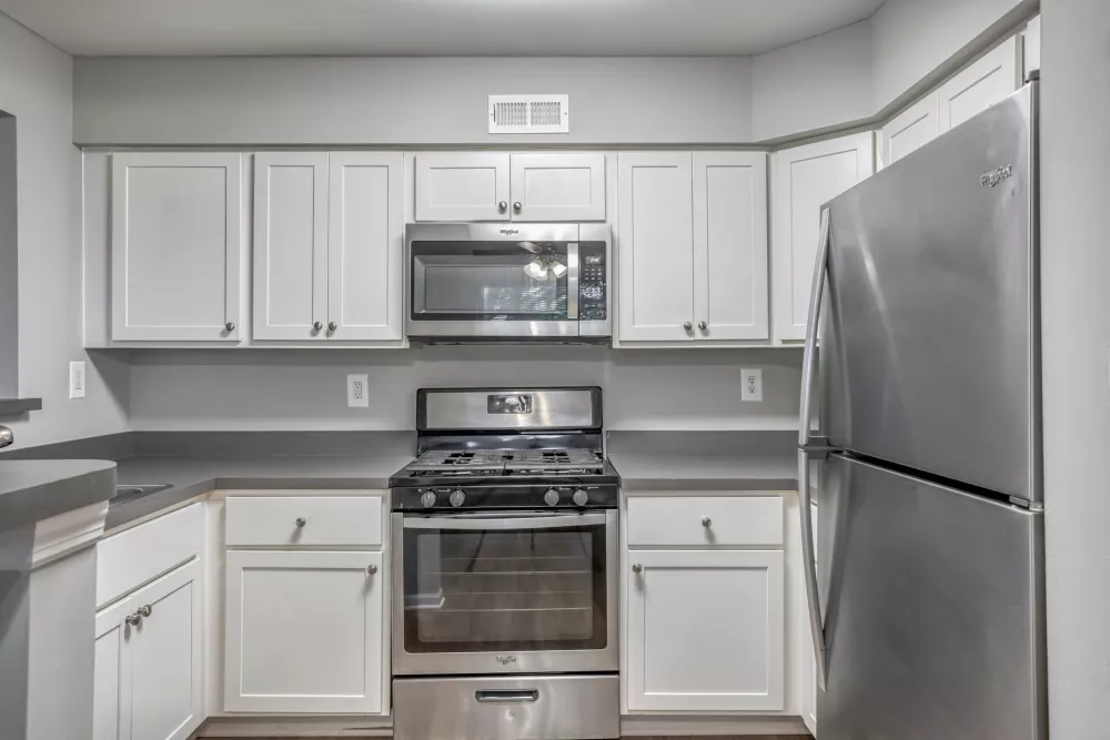 Modern kitchen with white cabinetry, gray countertops, and stainless steel refrigerator, gas range, and microwave.