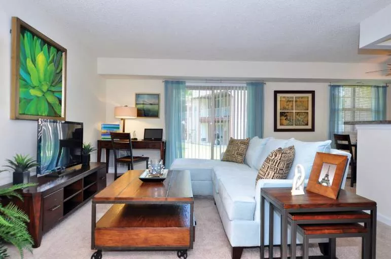 Bright living room with light blue sectional, dark wood furniture, green abstract art, and sliding glass doors to patio.