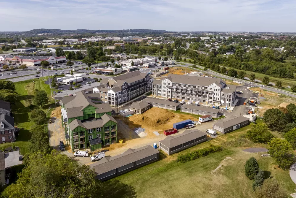 Aerial photograph: Residential complex under construction, with multi-story buildings, one featuring green siding, amidst dirt and temporary structures.