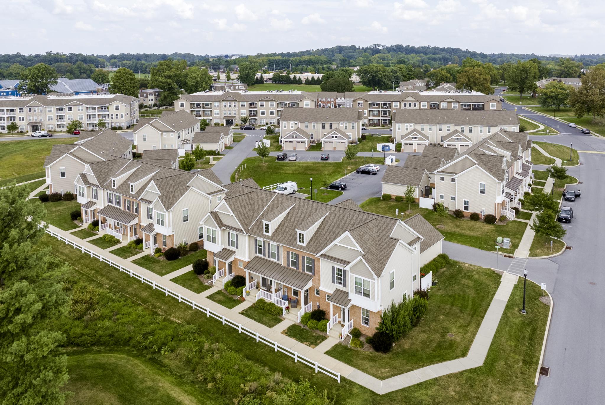 Drone view of newly built townhomes with private entrances, driveways, and garages set along landscaped streets.