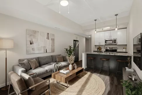 Photograph of a modern open-concept living room with grey sofa, armchairs, and a kitchen with white cabinets and dark island.