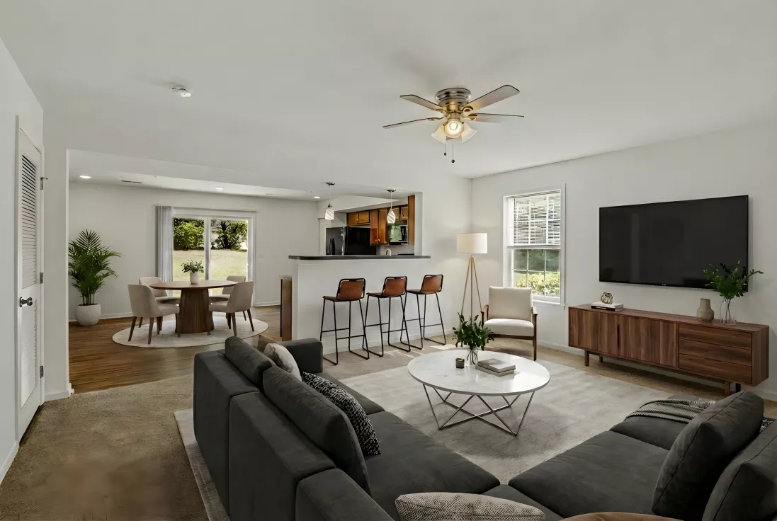 Spacious living room with gray sectional, round coffee table, TV, kitchen island, and dining area.