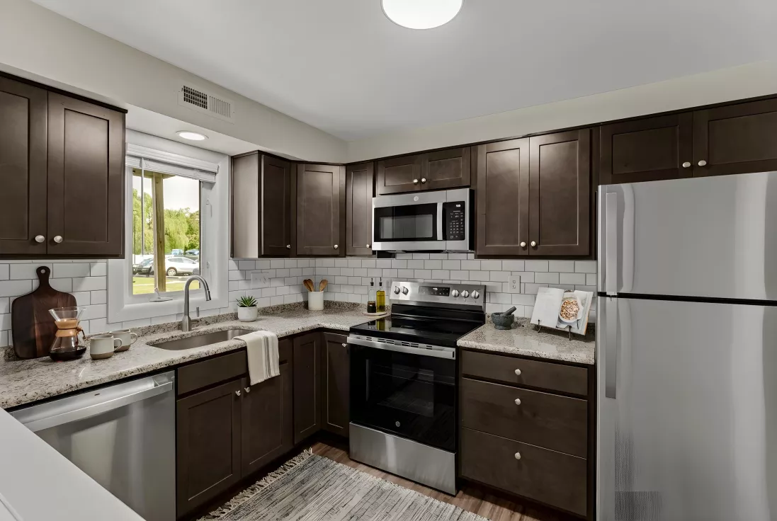 Modern kitchen with dark brown cabinets, stainless steel appliances, light granite countertops, and white subway tile backsplash.