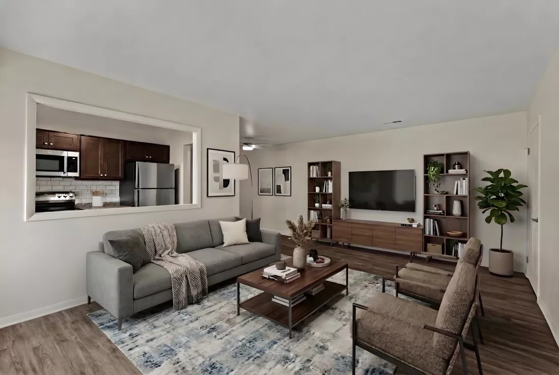 Modern living room with a gray sofa, coffee table, TV, bookshelves, and two armchairs. Kitchen seen through a wall cutout.