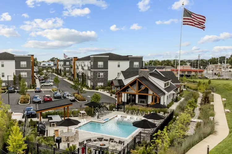 Photograph: Modern apartment complex with a swimming pool, clubhouse, and buildings, under a blue sky. An American flag flies high.