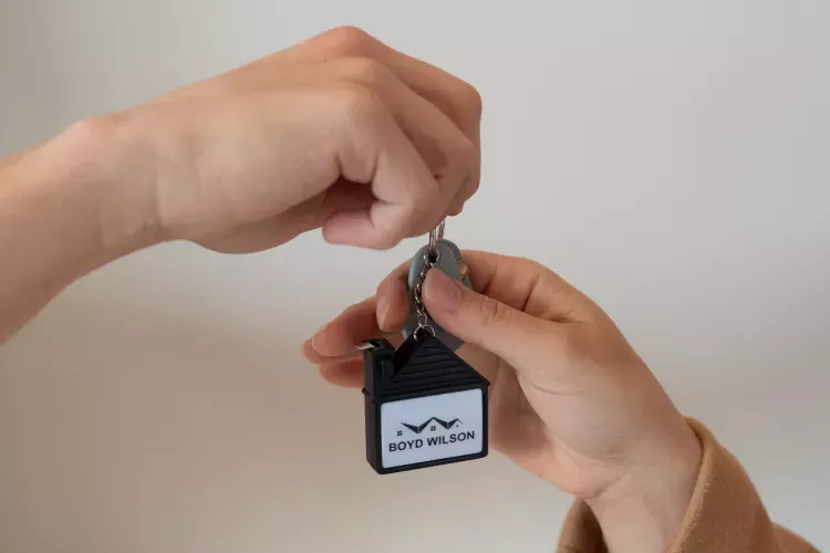 Hands exchanging a set of keys, one with a black house-shaped keychain.