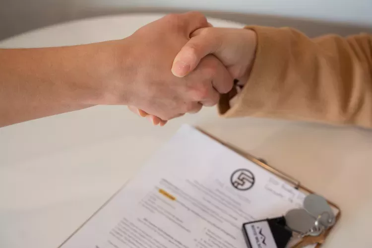 Photograph: Two hands shaking above a clipboard with a document and keys on a table.