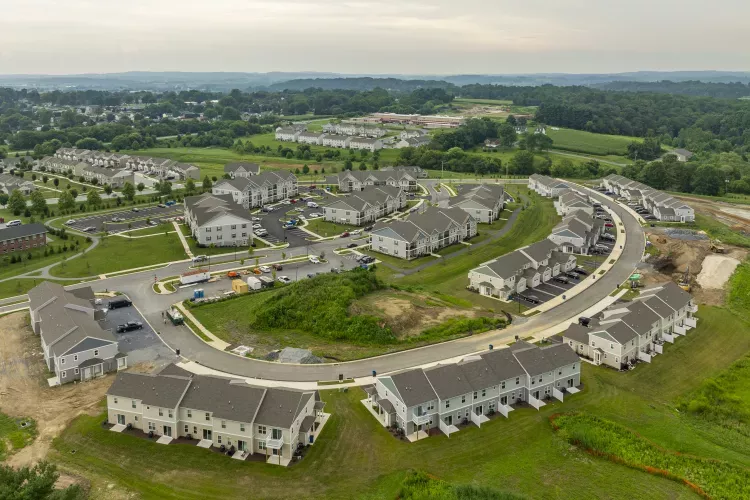 Aerial view of a new suburban development with grey-roofed townhouses and apartment buildings, some under construction.